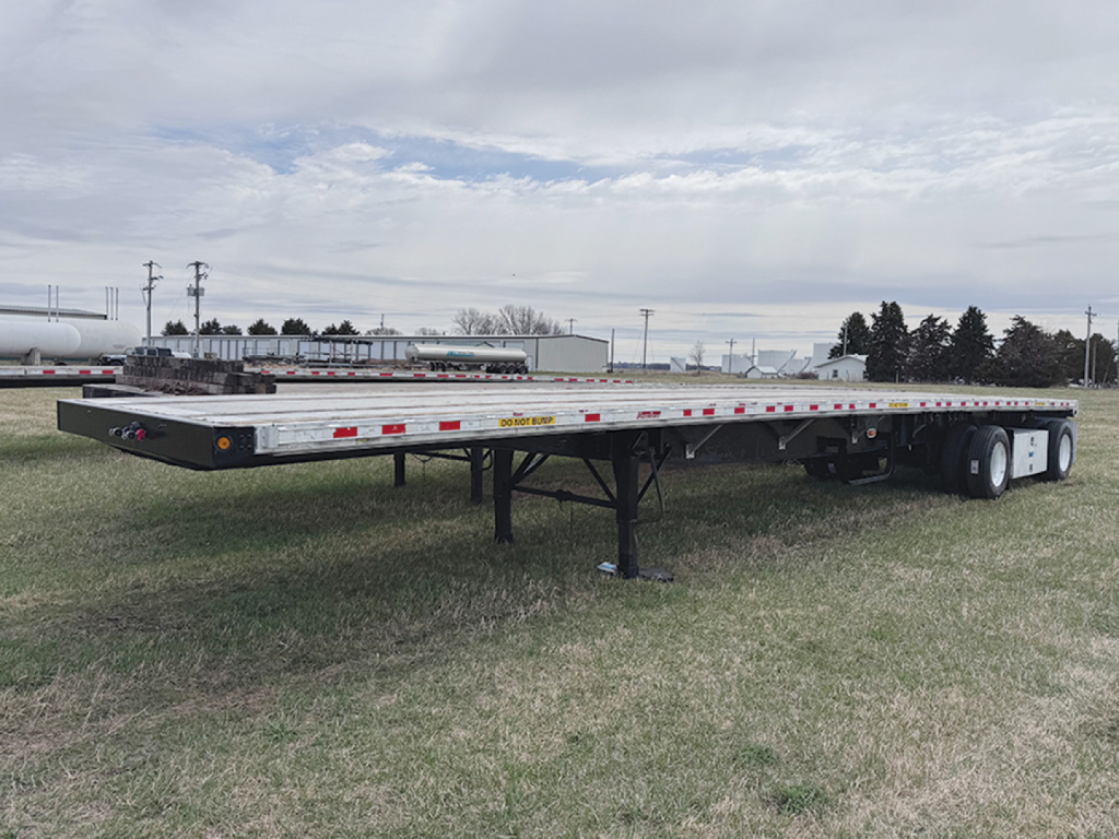 Great Dane flatbed trailer on grass with aluminum and steel composite deck, front landing gear down, rear dual axles, reflective tape along sides.