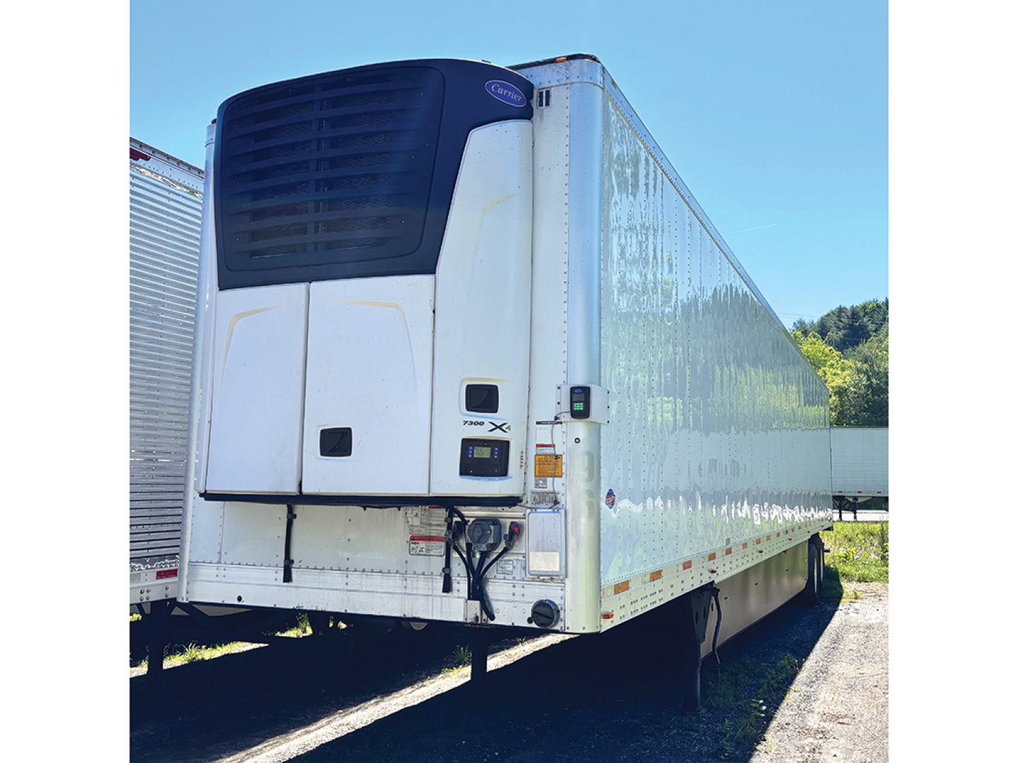 Reefer trailer by Utility 3000R with rear refrigeration unit and white body, side view showing plug-in connections and hitch.