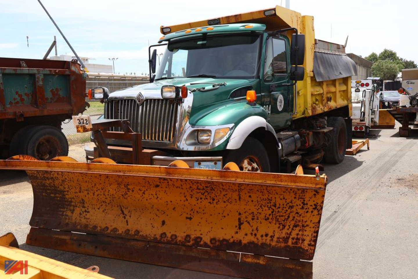 2007 International WorkStar 7400 dump truck with green cab and yellow dump bed, front chrome grille, and snow plow attachment in the foreground.