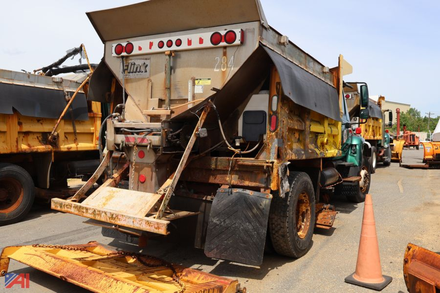 Dump truck rear view showing International WorkStar 7400 bed with tailgate and hydraulic hoist, rusty in-service appearance, rear lights, and orange cones nearby.