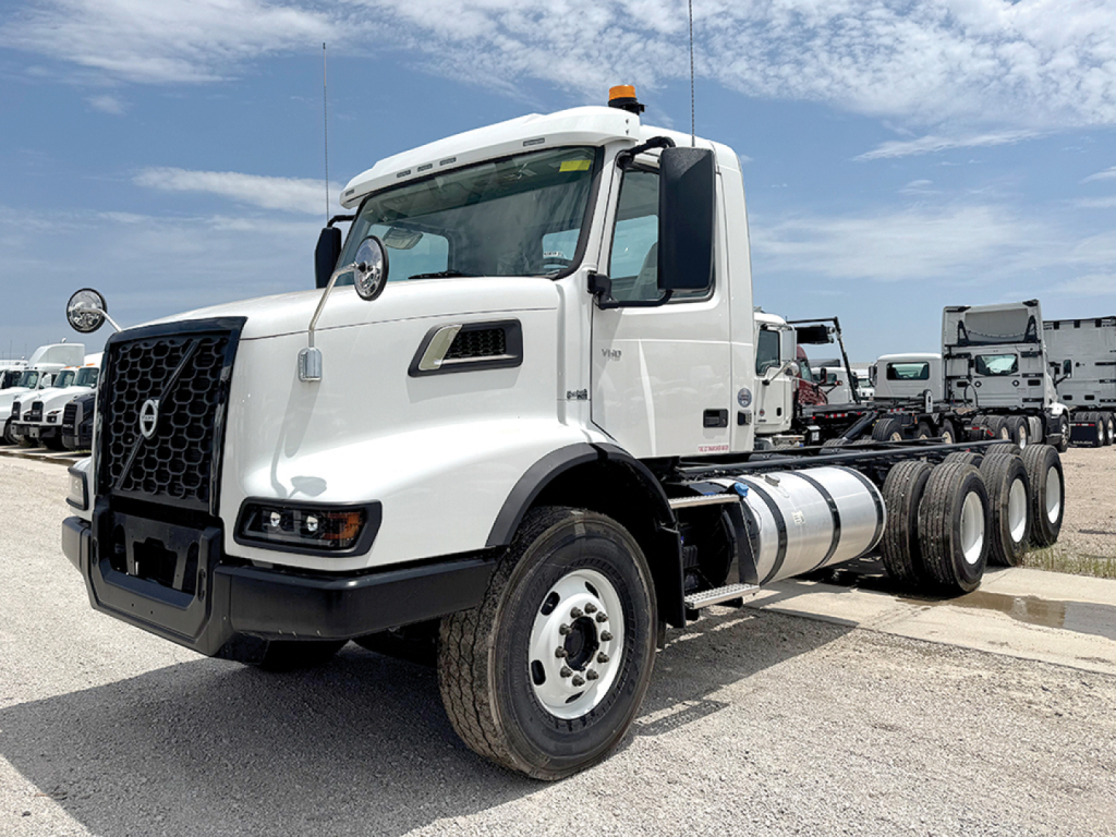 Volvo VHD 300 conventional daycab tractor in white, front-left view, showing fuel tanks, dual rear axles, and mounting hardware.