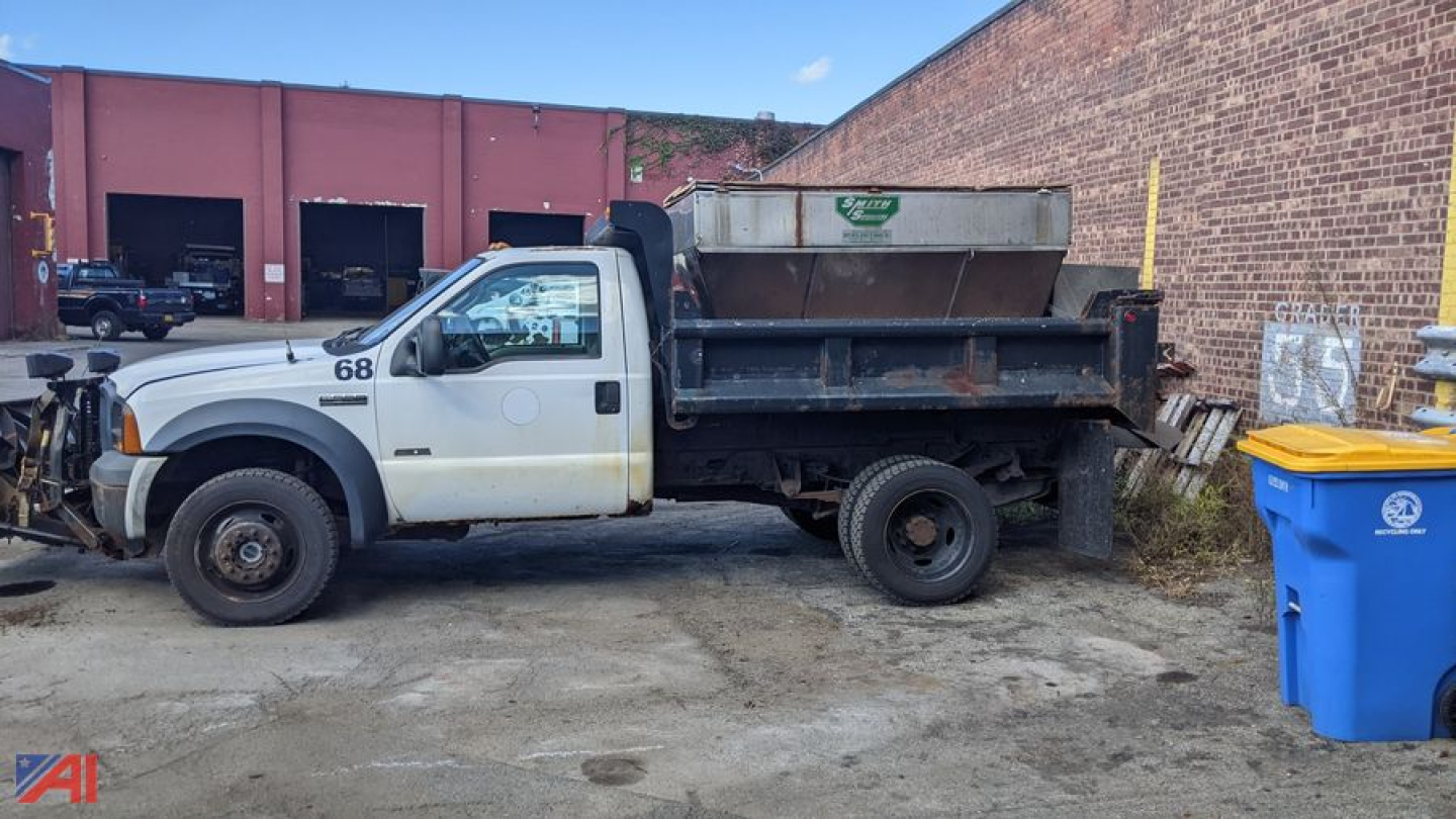 2006 Ford F-550 Super Duty dump truck with plow and sander, white cab, black dump bed, side view, number 68 on door, parked beside brick building.
