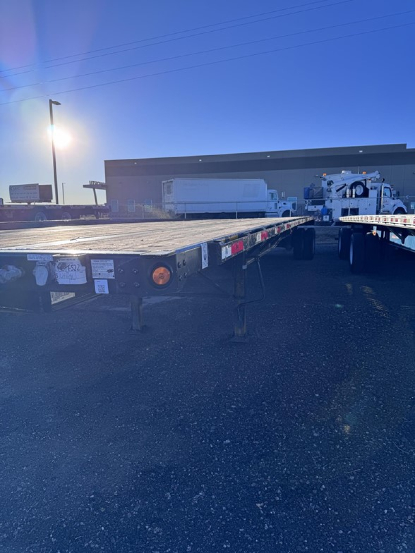 Flatbed trailer: 48' steel closed tandem with slider, viewed from rear-left side showing deck, side chain hooks, and rear lighting.