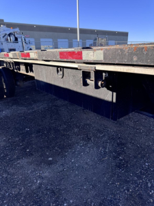 Flatbed trailer side view showing undercarriage and deck edge with stake pocket area and reflective tape, utility trailer equipment