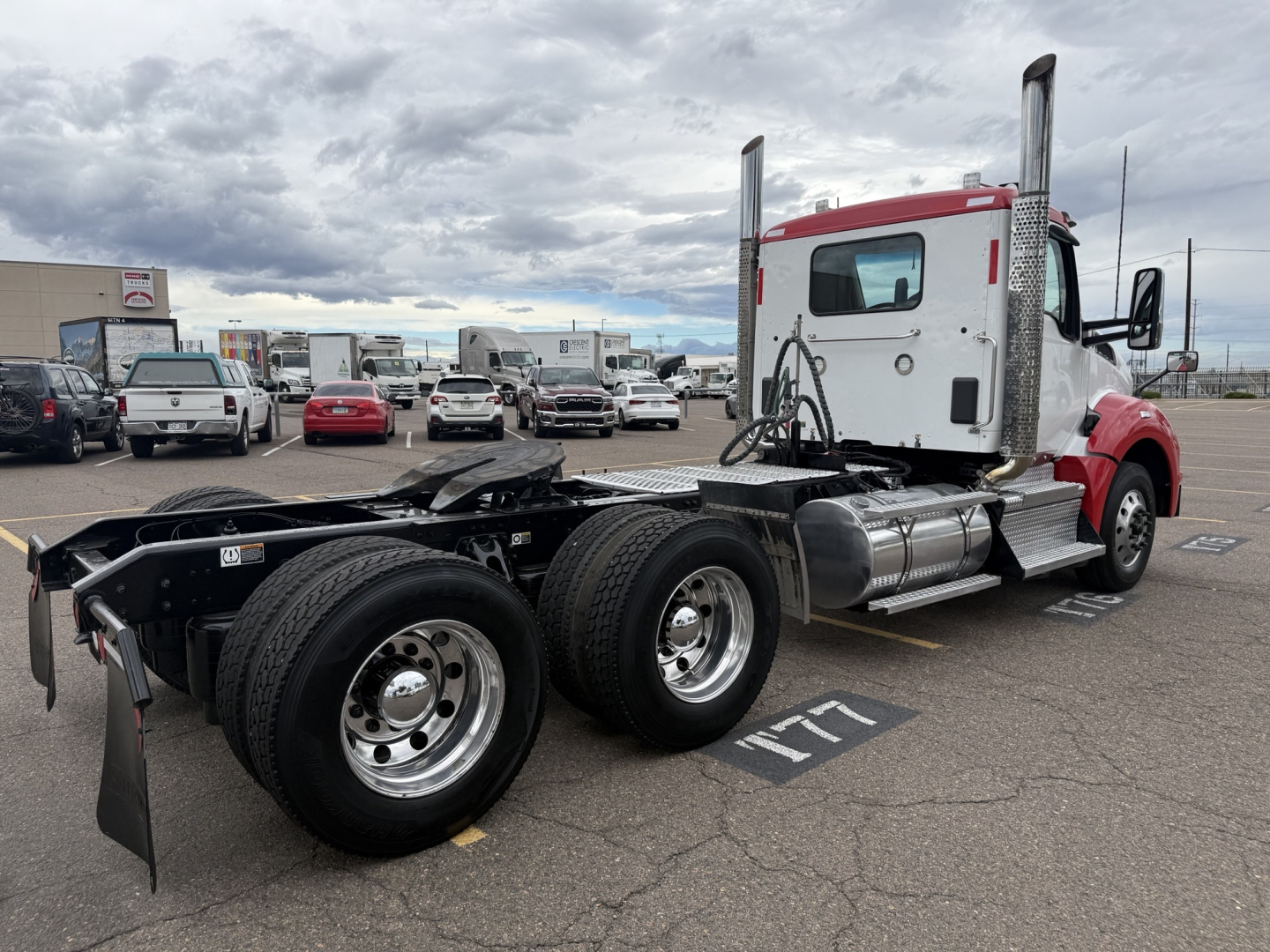 Kenworth T880 conventional daycab tractor from a side rear angle showing dual rear axles, fuel tanks, exhaust stacks, and cab with red and white paint.