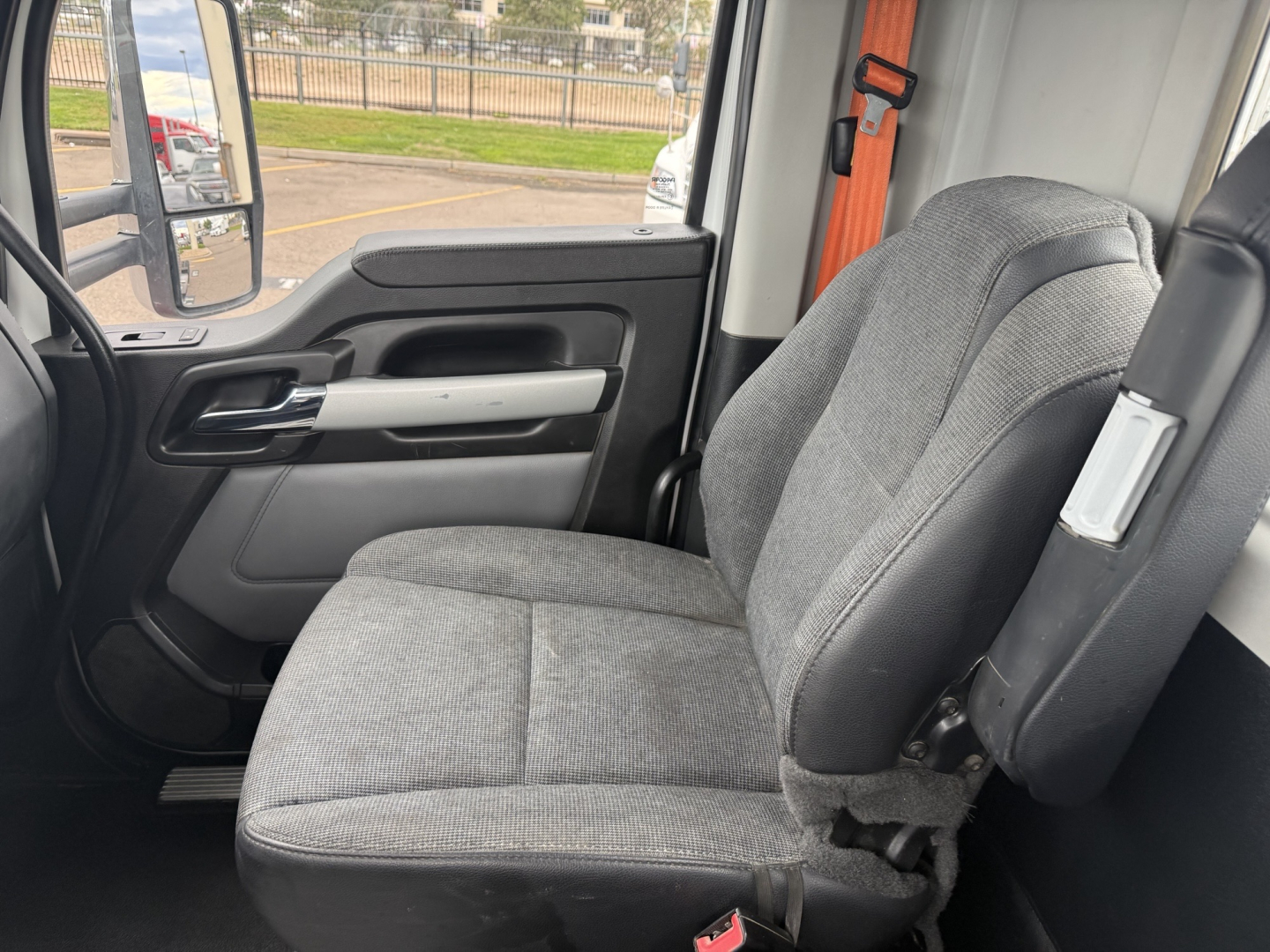Kenworth T880 cab interior with driver's seat, door panel, and seatbelt in view; partial exterior side mirror visible through window.