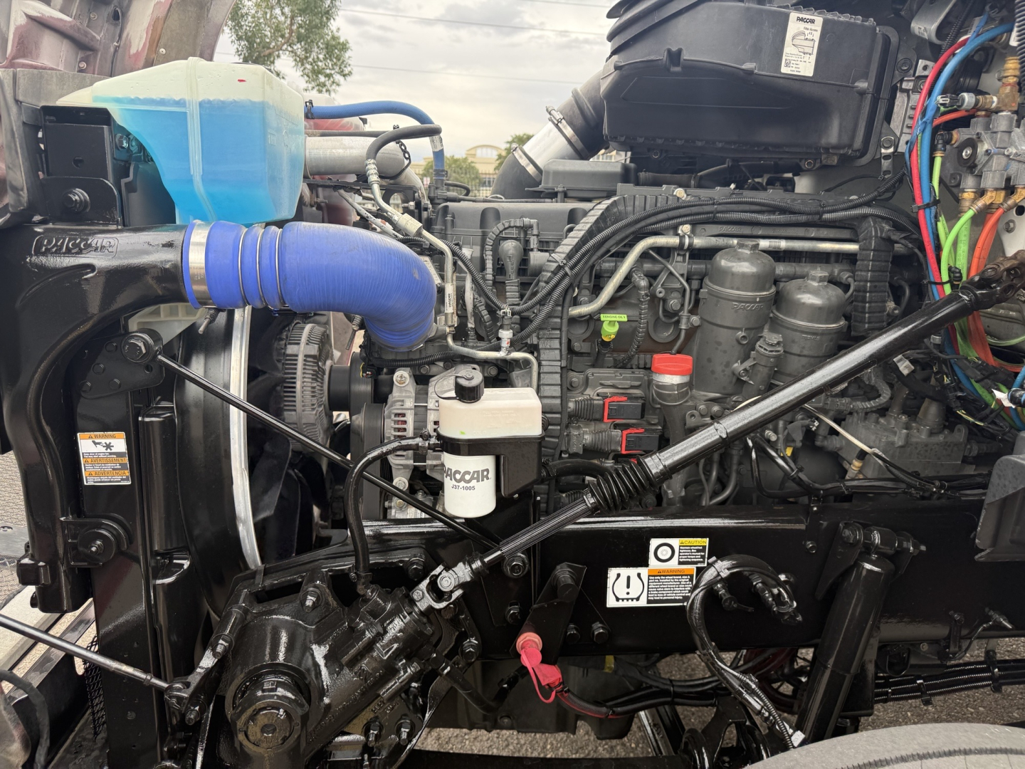 Kenworth T880 engine bay showing blue coolant hose, air intake, and various engine components with wiring and labels visible.
