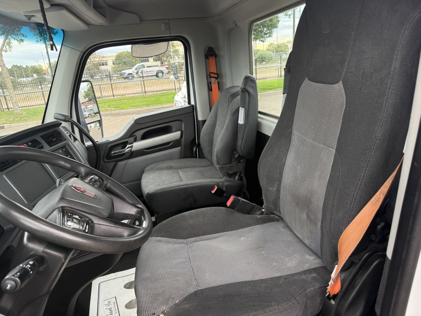 Kenworth T880 truck interior showing driver and passenger seats, steering wheel, dash, and side window view.