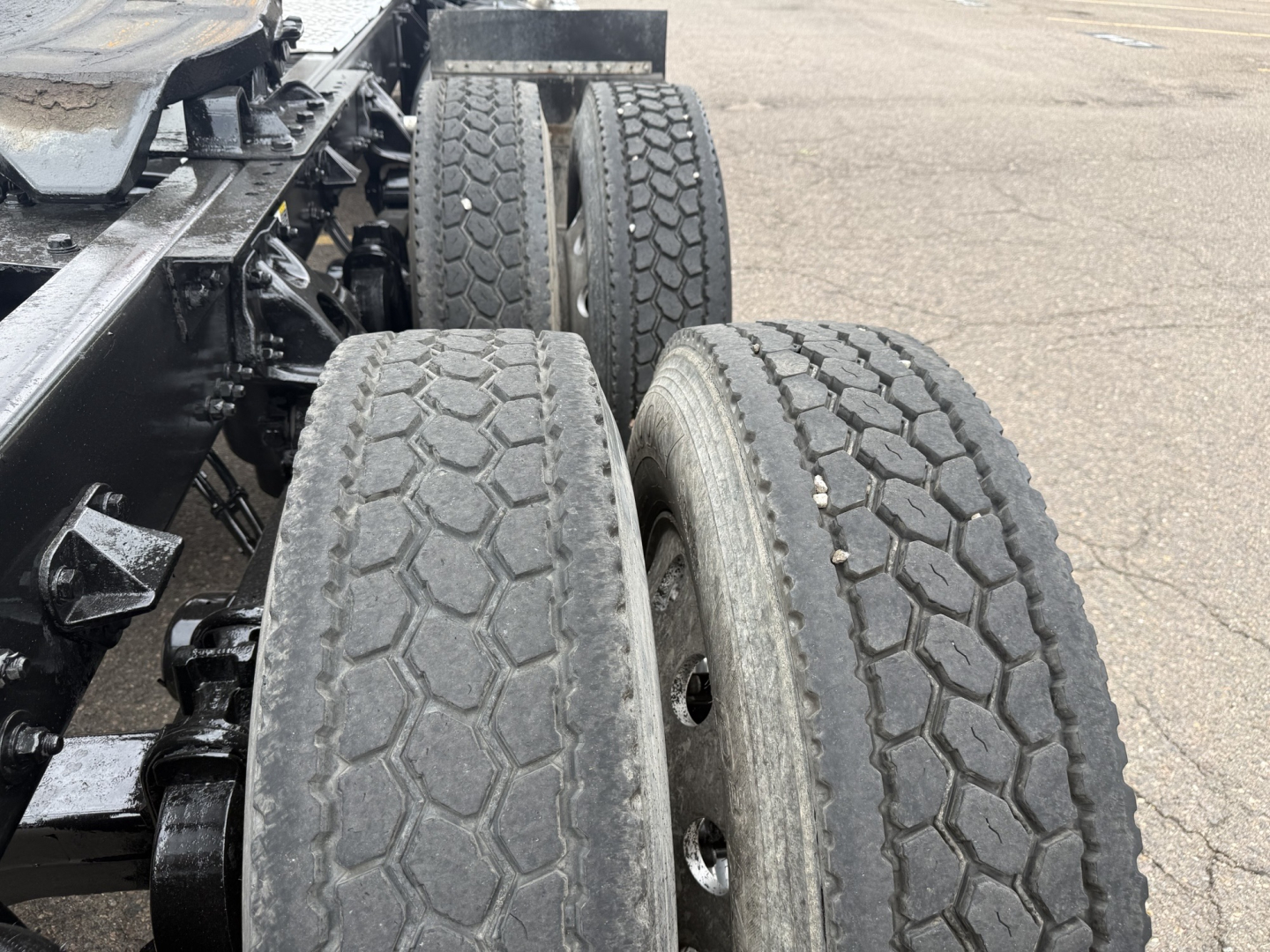 Kenworth truck chassis and dual rear wheels (tandem). Visible treaded tires on tandem axle with hexagonal tread pattern; chassis framing and suspension components in view.