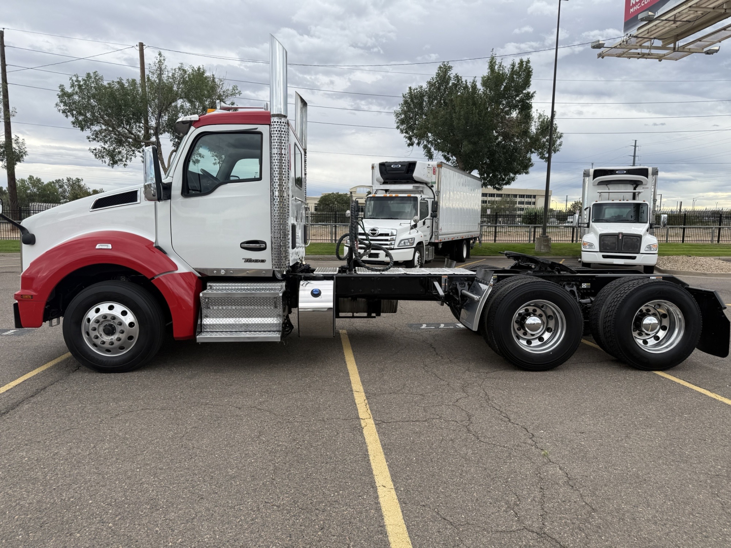 Kenworth T880 semi truck side view with white cab and red fender, chassis exposed, two rear axles, daytime parking lot.