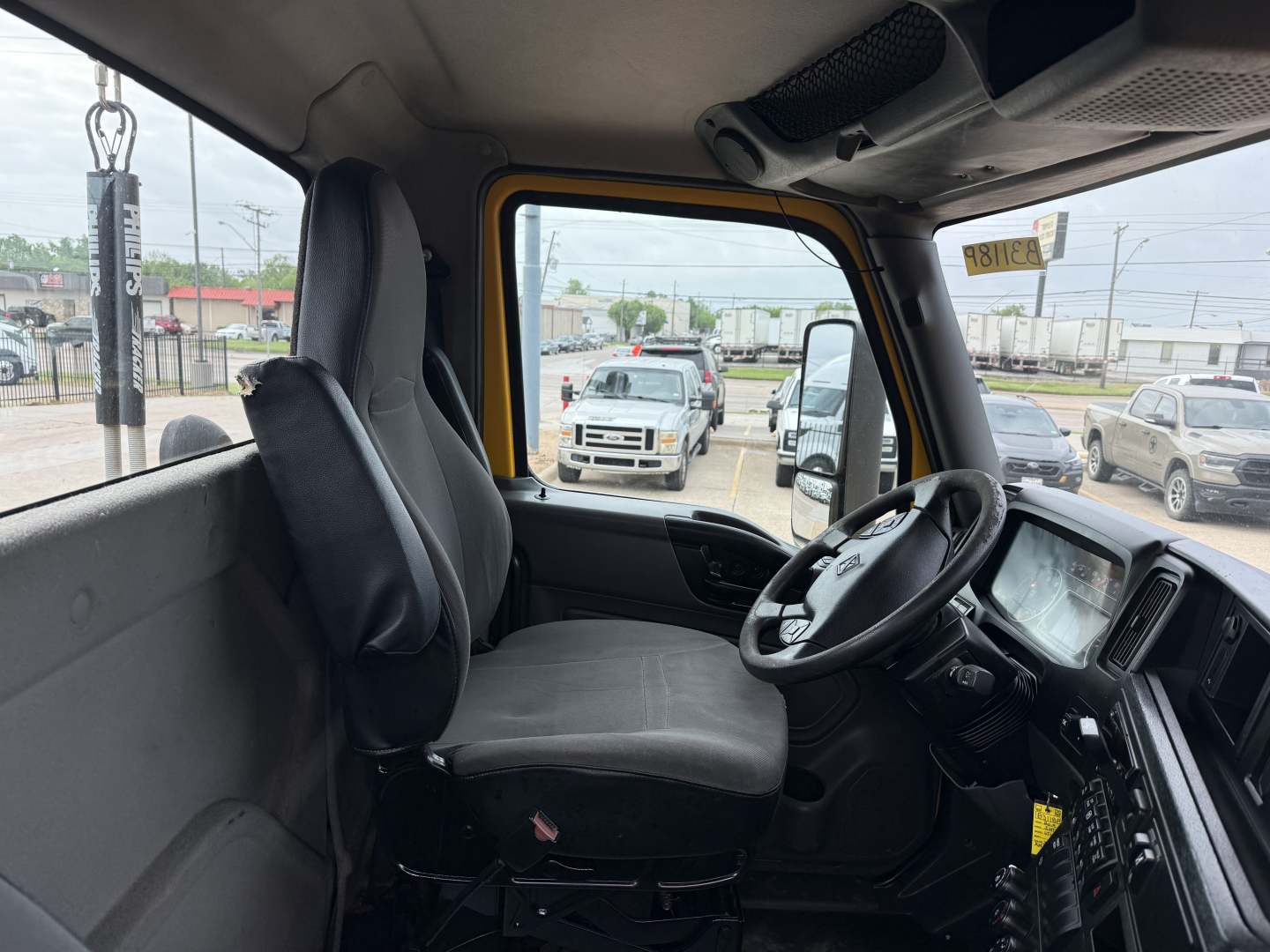Interior of a 2019 International LT truck cab showing driver seat, steering wheel, and dashboard from the passenger side; door window reflects a dealership lot.