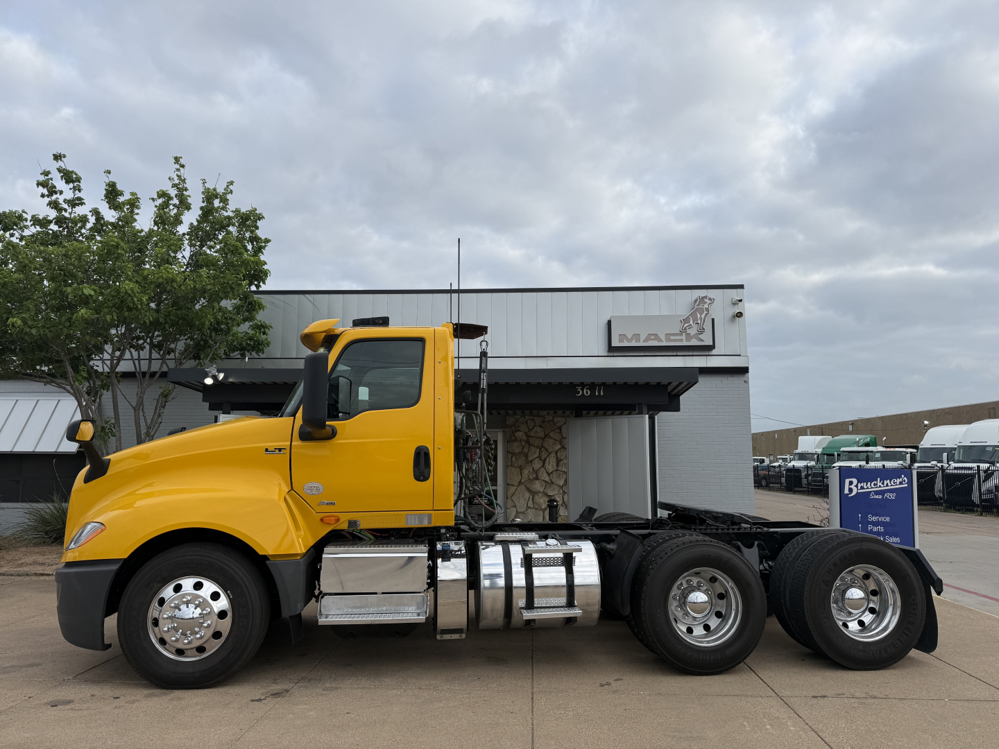 Truck side view showing a bright yellow 2019 International LT cab with a beavertail 6x4 chassis and twin rear axles. Visible text includes VIN plate with 3HSDZTZR3KN739956 and a Brakes sign in the background.