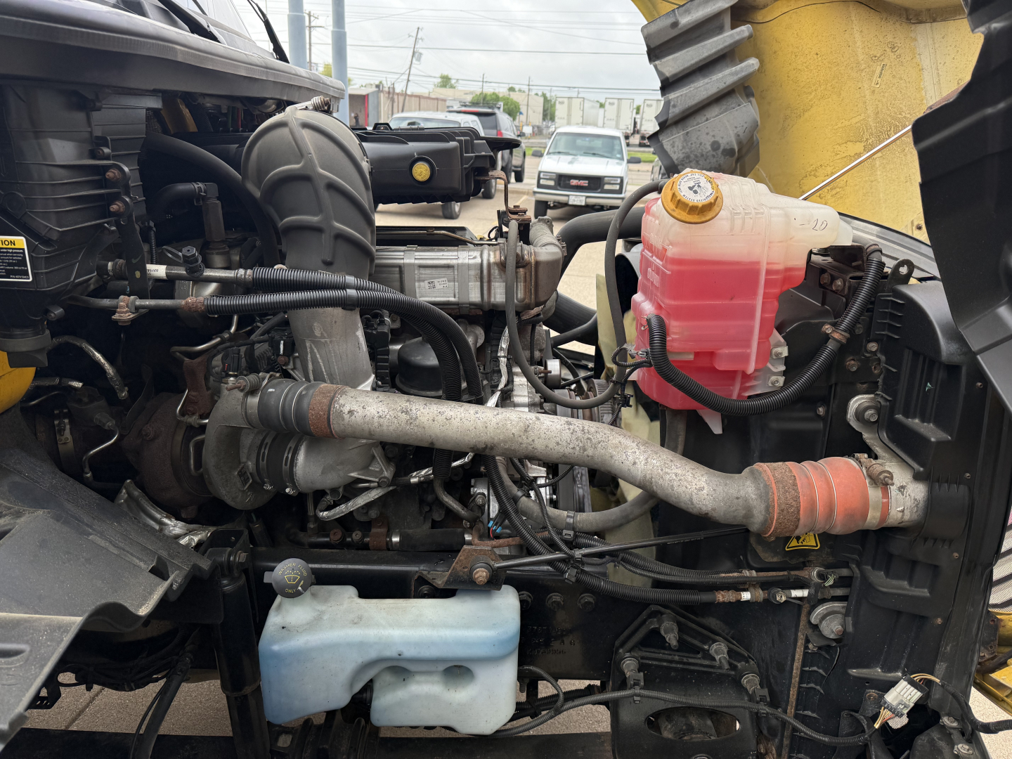 Engine bay of a 2019 International LT conventional daycab showing coolant reservoir, power steering/ hydraulic lines, and various hoses.