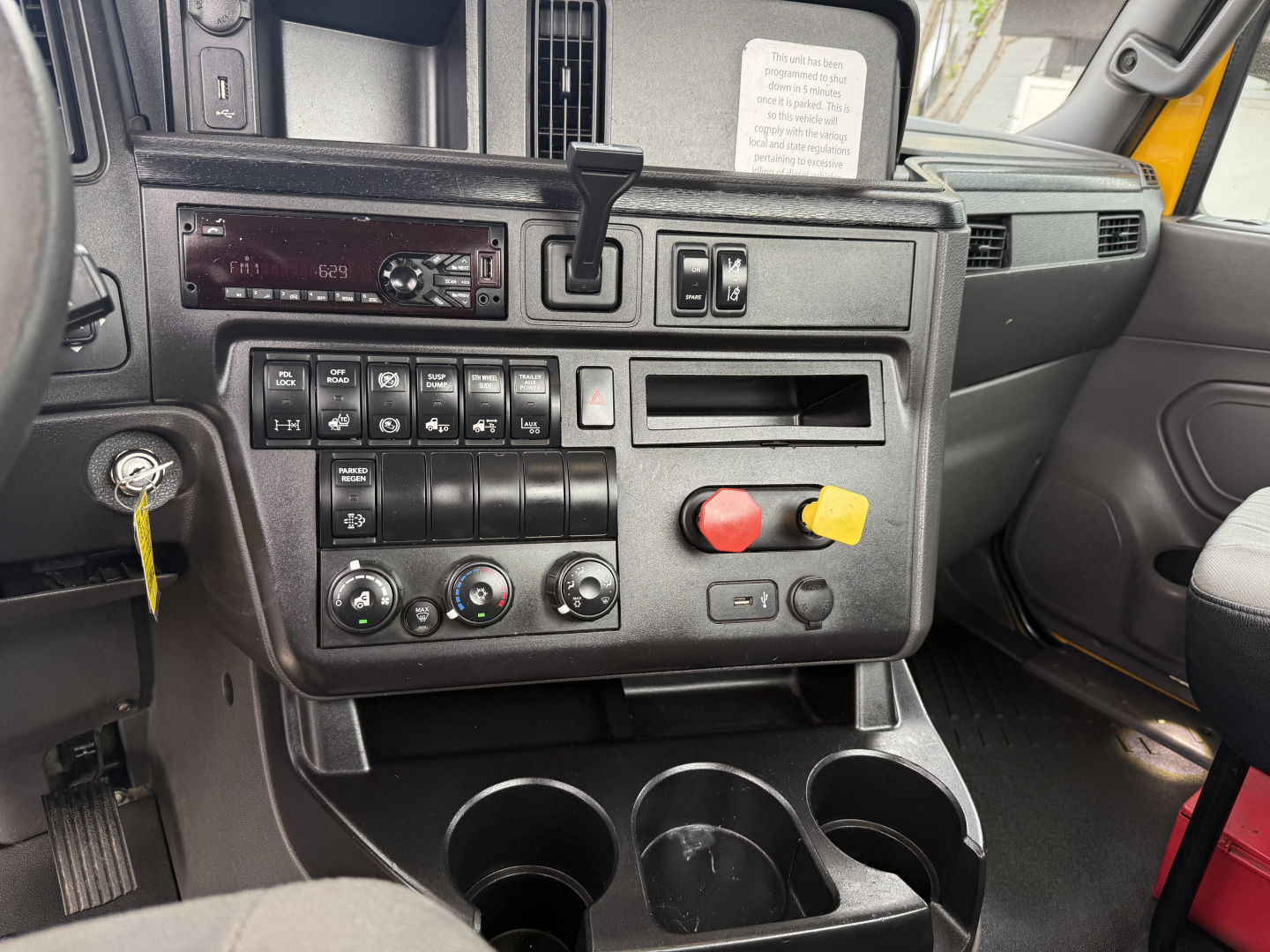 Interior dash of a 2019 International LT daycab showing controls, cup holders, and radio panel with knobs and switches; visible yellow and red push buttons near center console.