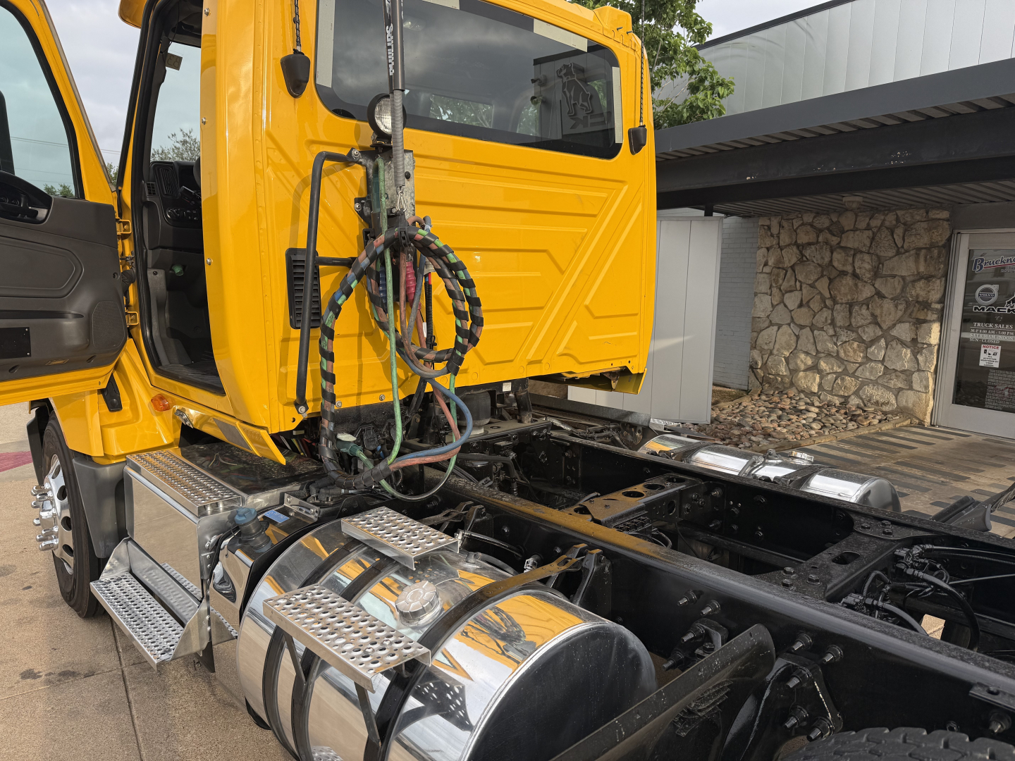Truck cab with open door showing yellow International LT diesel truck, exposed chassis, wiring, and chrome steps.