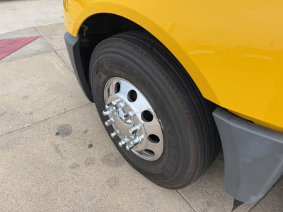 Truck wheel and front fender of a yellow 2019 International LT with chrome hubcap and tire, partial wheel well and mudguard visible.