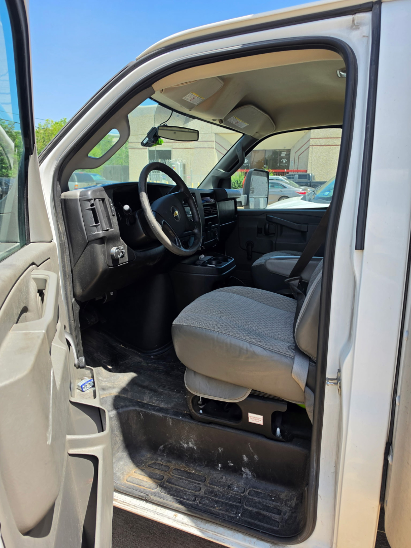 Front interior of a 2016 Chevrolet Express 3500 cargo van showing driver's seat, steering wheel, dashboard, and open entry with black floor mat.