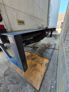 Trucks/box truck rear view showing loading dock with wooden platform and metal frame, mid-section of trailer undercarriage visible.