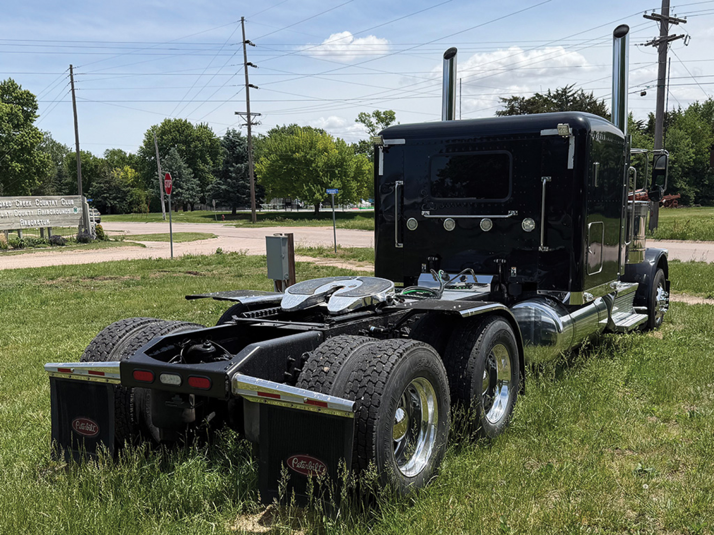 Peterbilt 389 extended hood tractor show rear and cab with dual rear axles, black paint, fuel tanks, and fifth wheel plate.