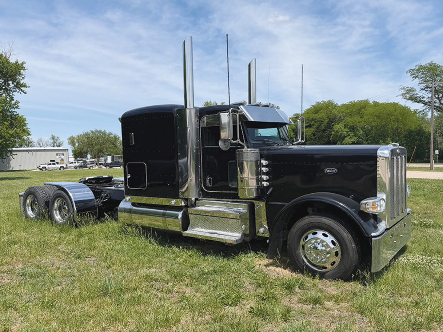 Peterbilt 389 extended hood conventional sleeper truck in black, with chrome accents, front grille, large dual exhaust stacks, and empty flatbed behind.