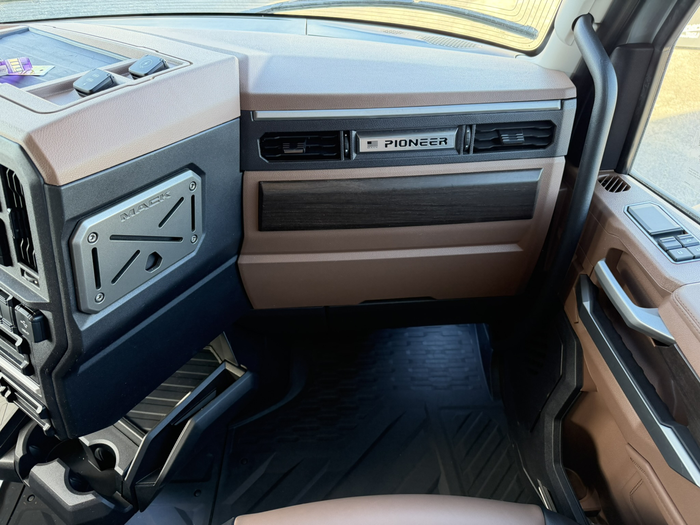 Cab interior of a 2026 Mack PR64T76H truck showing brown dashboard, Pioneer dash vent, and step footwell area.