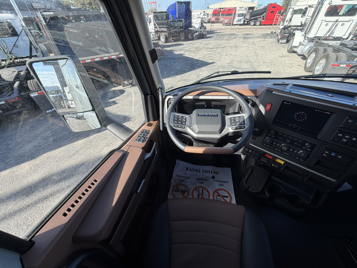 Cabin interior of a 2026 Mack PR64T76H truck showing steering wheel, dashboard, and driver's seat with brown trim.