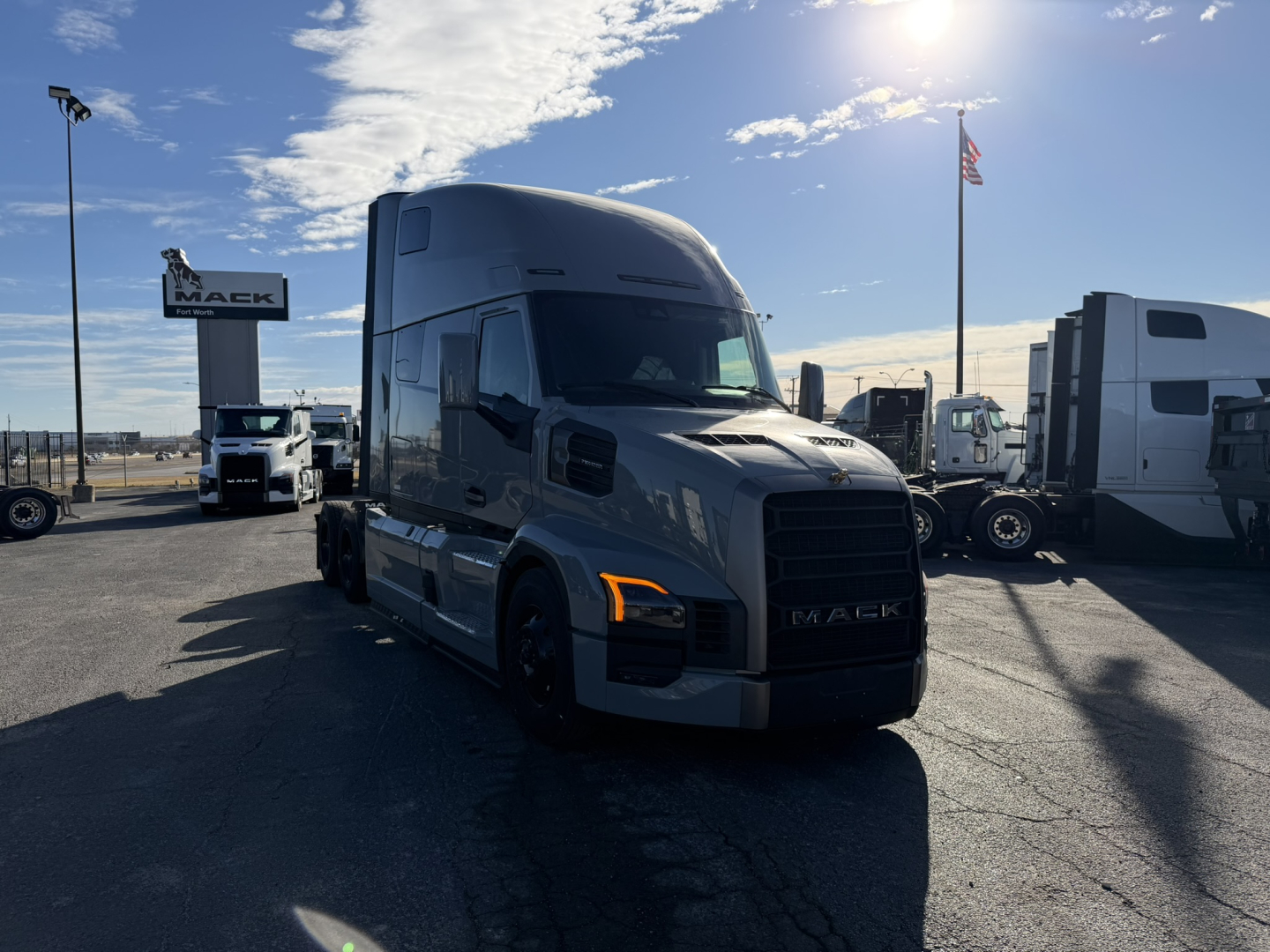 Mack PR64T76H conventional sleeper truck in a dealership lot, front-right view with other trucks in background.