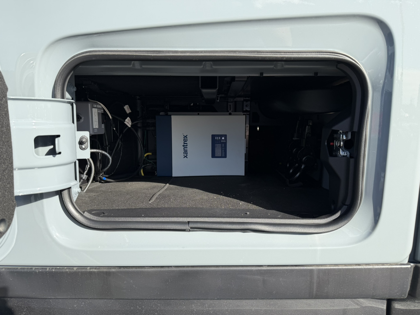 Truck cab storage showing a blue and white portable power unit or electrical component labeled 'Power' or 'Inverter' with cables around; side cabinet and dash area not fully visible.