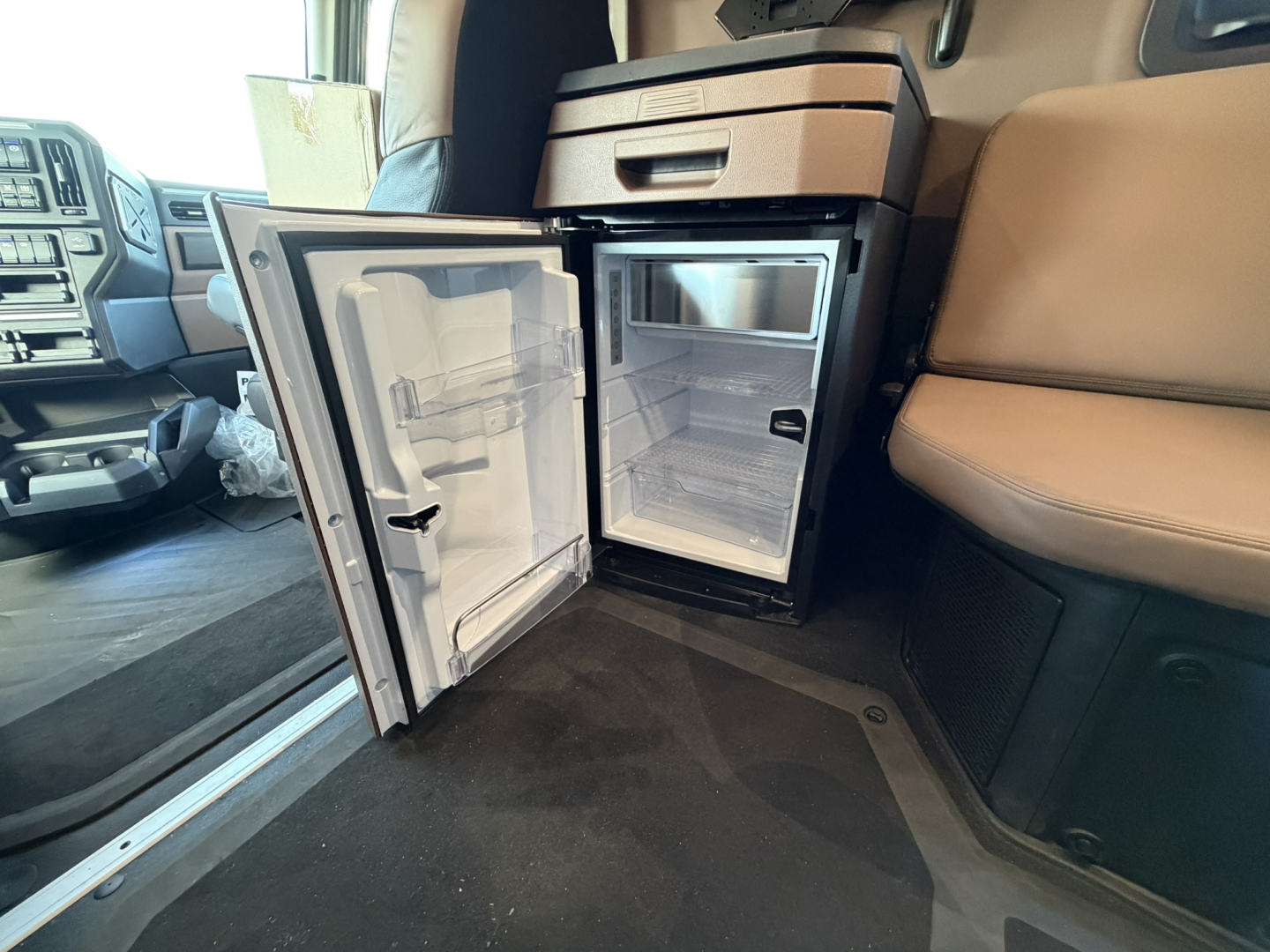 Mack PR64T76H conventional sleeper truck interior showing open under-dash fridge/freezer unit with small refrigerator compartments.