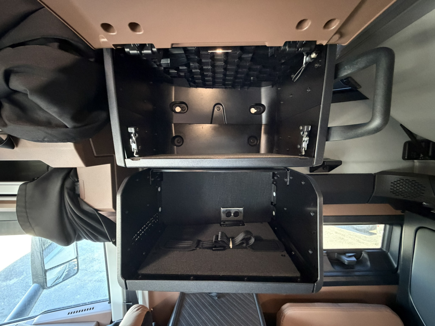 Mack PR64T76H cab interior with open overhead storage compartment and lower storage bay, view of dashboard and windshield area.