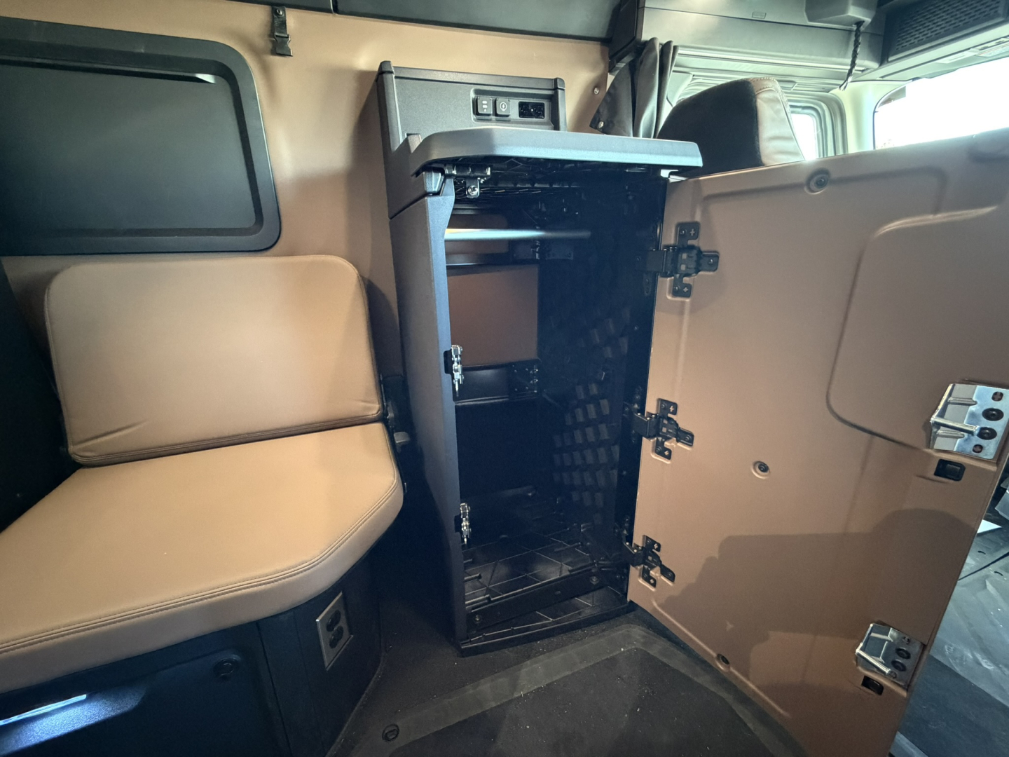 Truck cab interior showing open storage cabinet with shelves and latch hinges in a Mack PR64T76H.