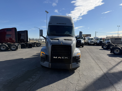 Mack PR64T76H tractor cab front view with bold grille and Mack emblem, headlights, and large side mirrors; clear blue sky.