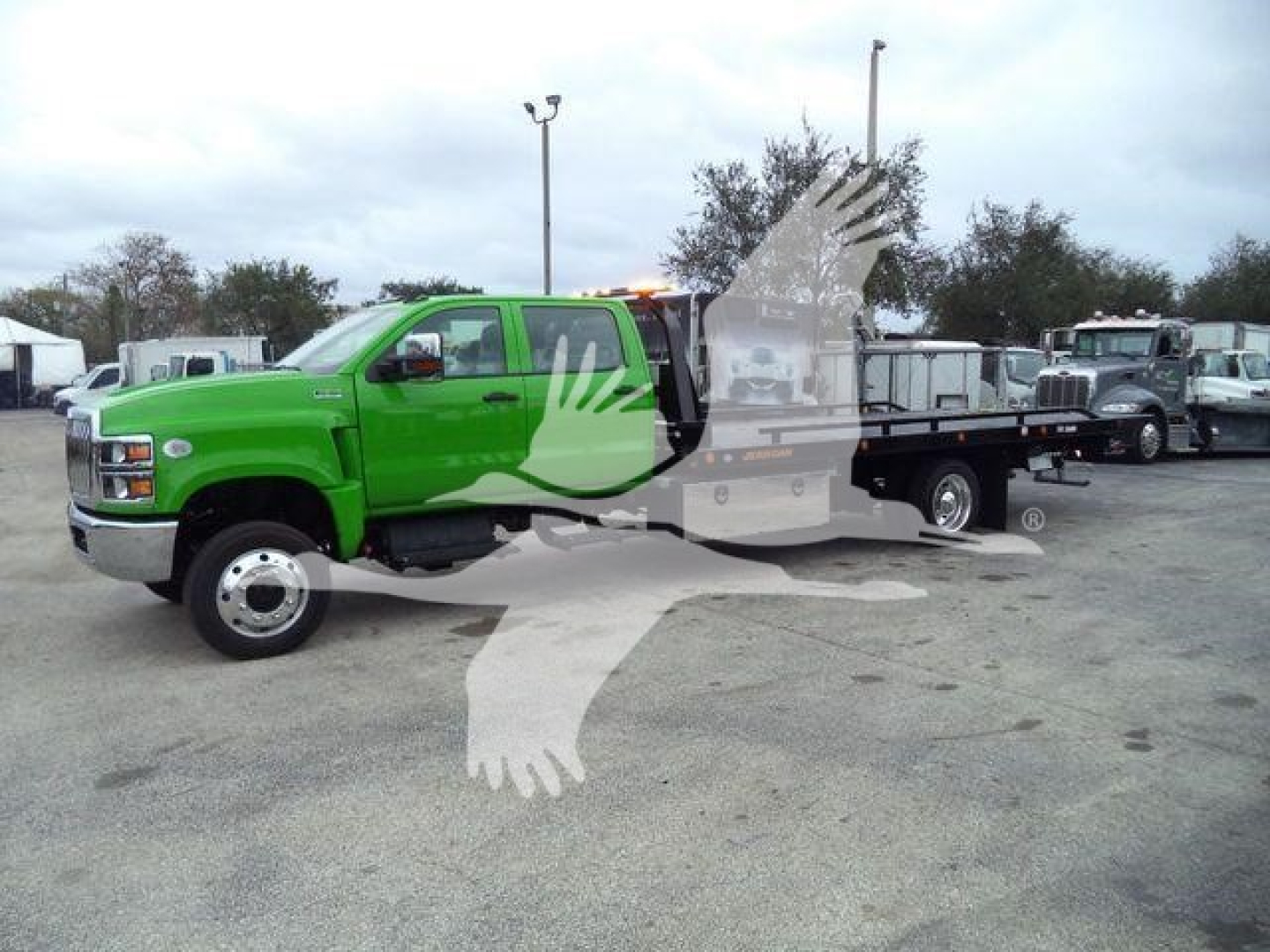 Green 2023 International CV rollback truck viewed from side with flatbed; stock background shows other trucks.