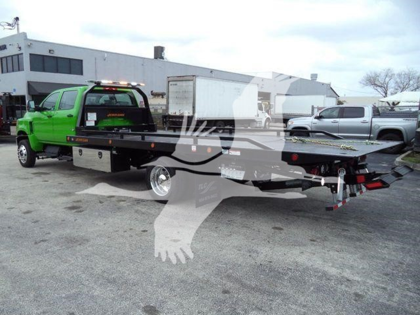 Flatbed tow truck with bright green cab and black steel bed, side view showing rollback equipment and hydraulic platform.