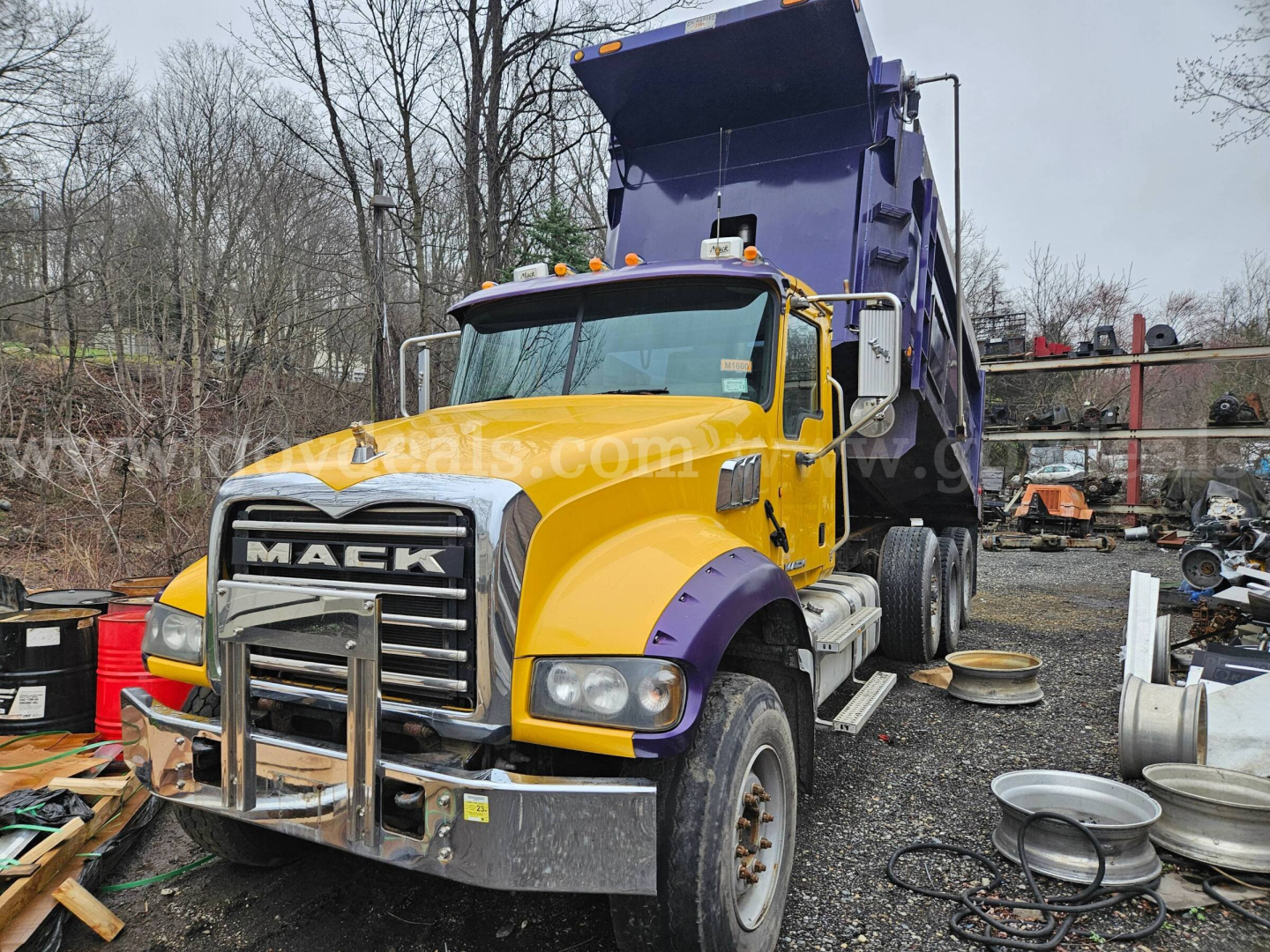 Mack GU713 dump truck in yard with yellow cab and purple dump, front grille guard visible