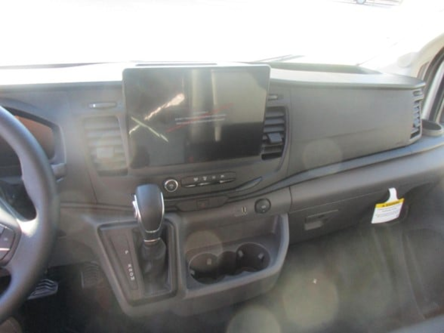 Interior of a new 2026 Ford Transit cargo van showing dashboard with large central touchscreen, gear selector, and cup holders.