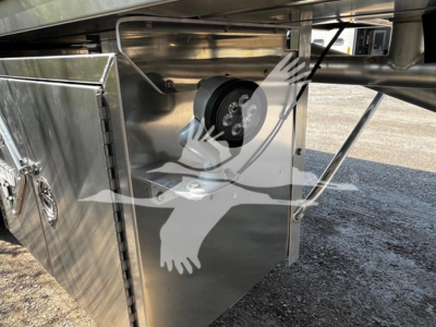 Under-trailer equipment box with a circular black component mounted inside, stainless steel paneling, bracketry, and hoses visible.