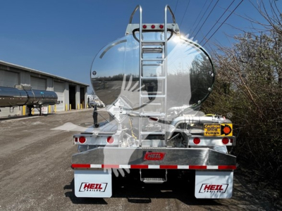 Rear view of a polished aluminum Heil 4-comp trailer with a ladder on the tank, safety decals, and red/white reflective tape.
