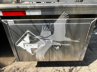 Trailer storage compartment with two stainless steel doors; diamond-shaped warning placard and circular lock visible.