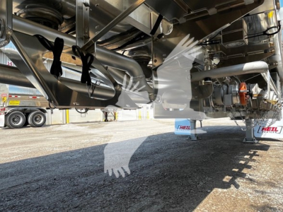 Trailer undercarriage showing structural beams, suspension, and piping of a Heil 4-Comp trailer with visible hydraulic lines and landing gear.