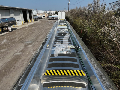 Top view of a long Heil 9500 gallon trailer looking down the center, with metal frame, reflective surface, and yellow-black caution stripes along the edges.
