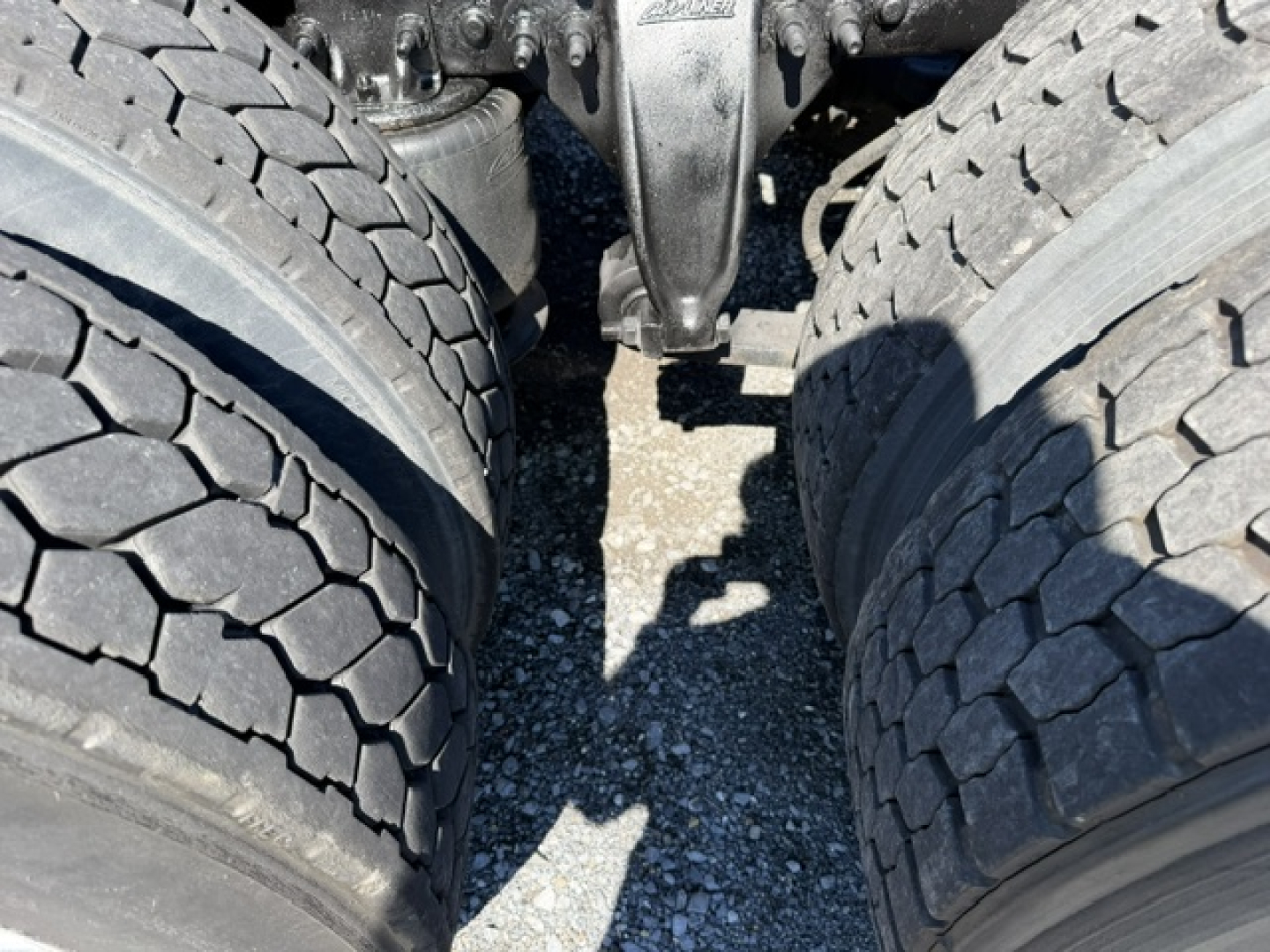 Truck drivetrain view showing tandem rear axles and dual tires of a Freightliner Cascadia CA125DC.