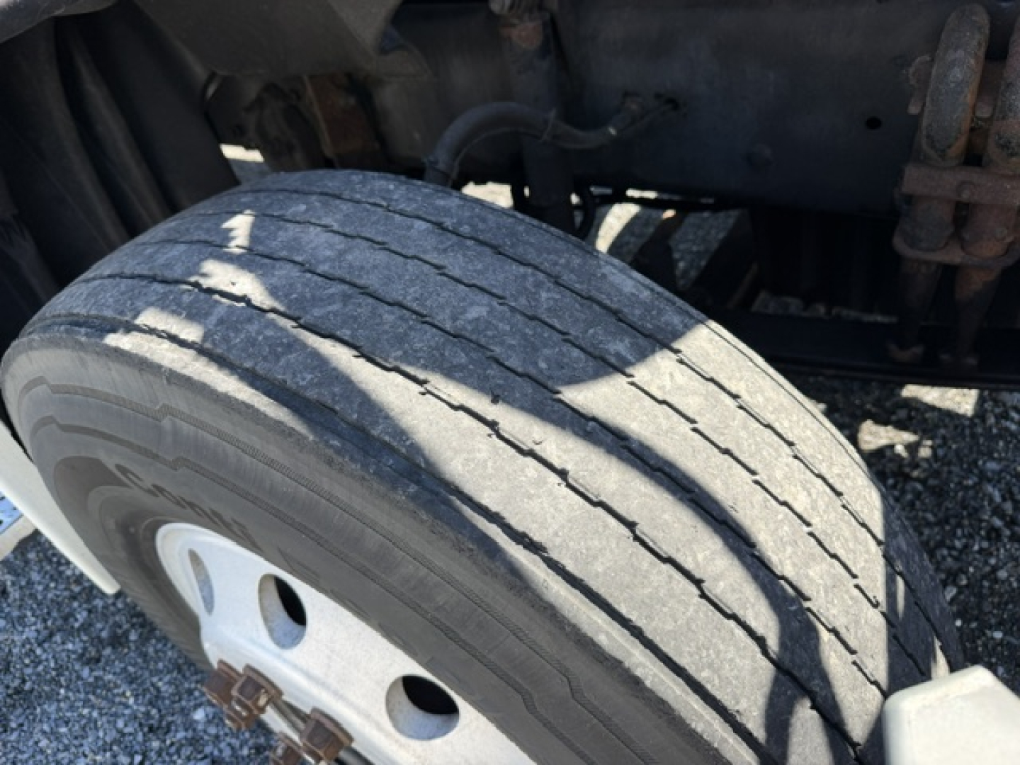 Rear wheel and suspension area of a Freightliner Cascadia truck showing a worn front tire tread and wheel hub; partial chassis and components visible.