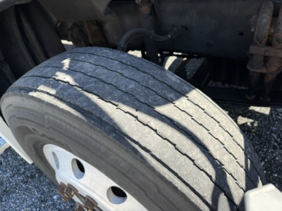 Rear wheel and suspension area of a Freightliner Cascadia truck showing a worn front tire tread and wheel hub; partial chassis and components visible.