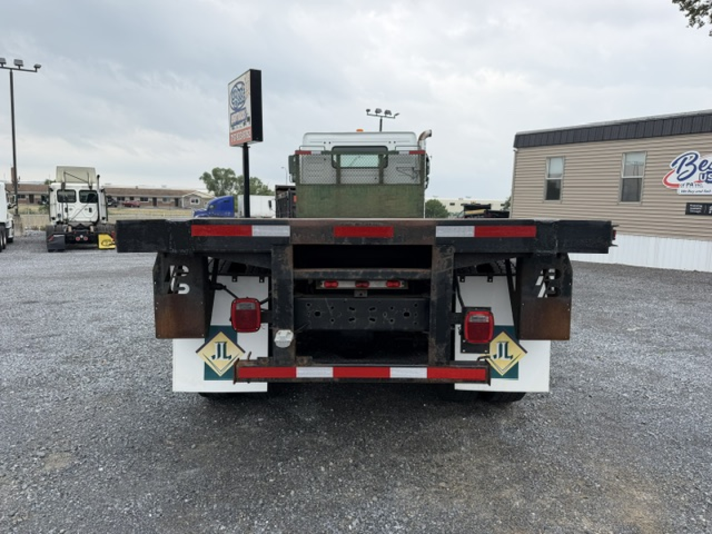 Rear view of a 2006 Volvo VHD flatbed truck showing taillights, reflectors, and bumper with safety decals. Flatbed bed and metal supports visible.