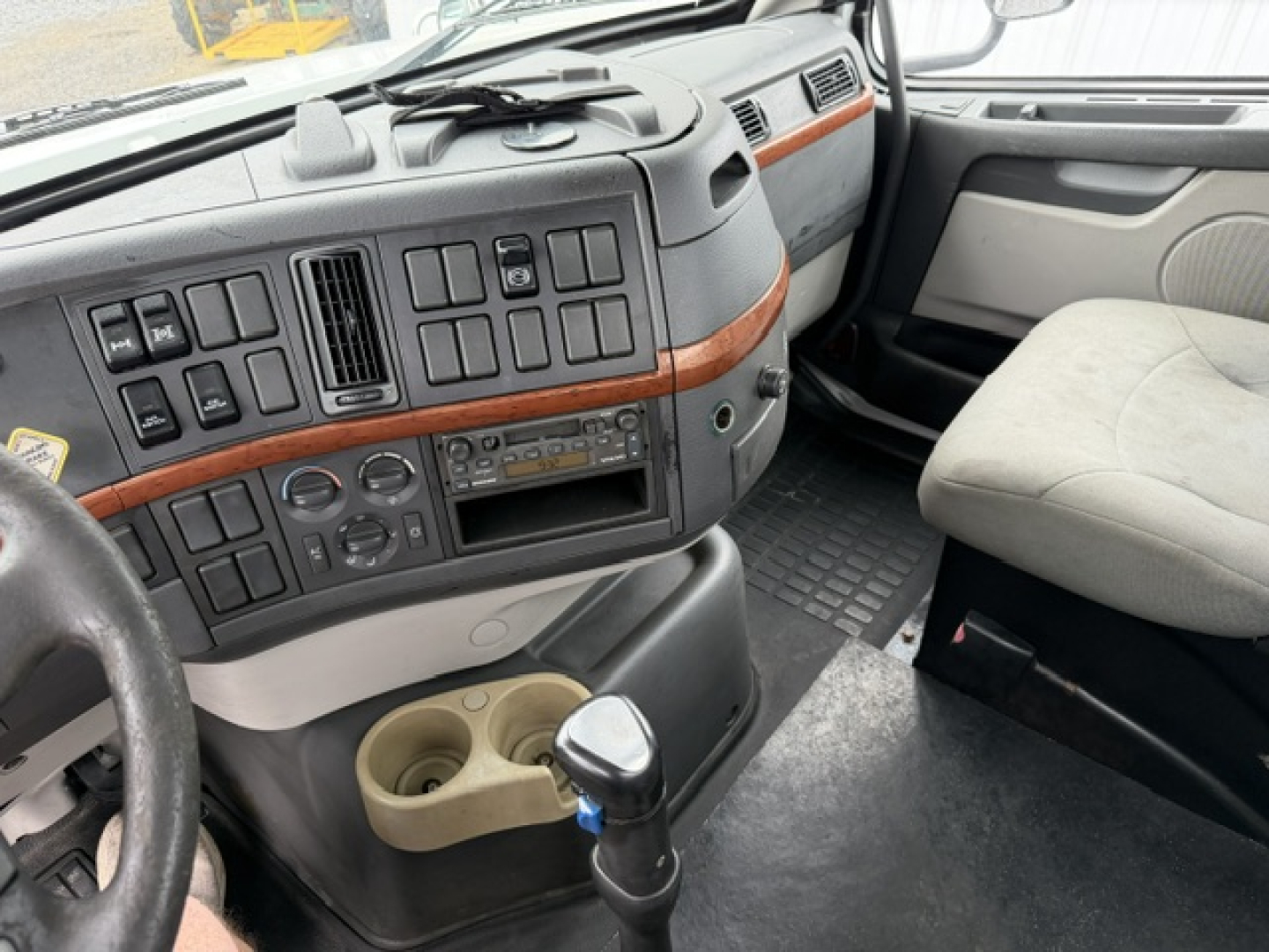 Volvo VHD cab interior showing dashboard with multiple switches, wooden trim, cup holders, and gear shifter in view.