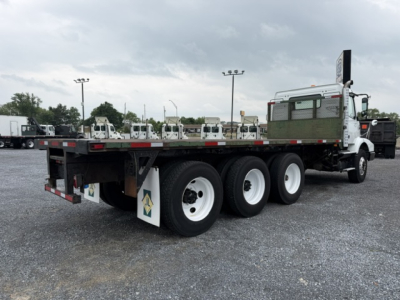 Flatbed tow truck with five-axle configuration showing white wheels, green flatbed, and side markers; Volvo-focused cab in white with a sleeper and exhaust stack.