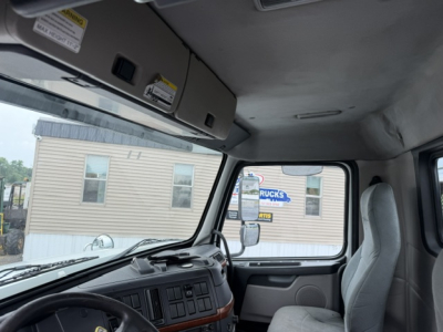 Truck cab interior showing dashboard, steering wheel, and driver seat of a Volvo VHD with overhead storage and windshield view.