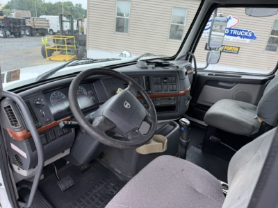 Interior of a Volvo VHD truck cab showing steering wheel, dashboard, and driver seat with gray fabric; dashboard features wood-grain trim and control cluster.