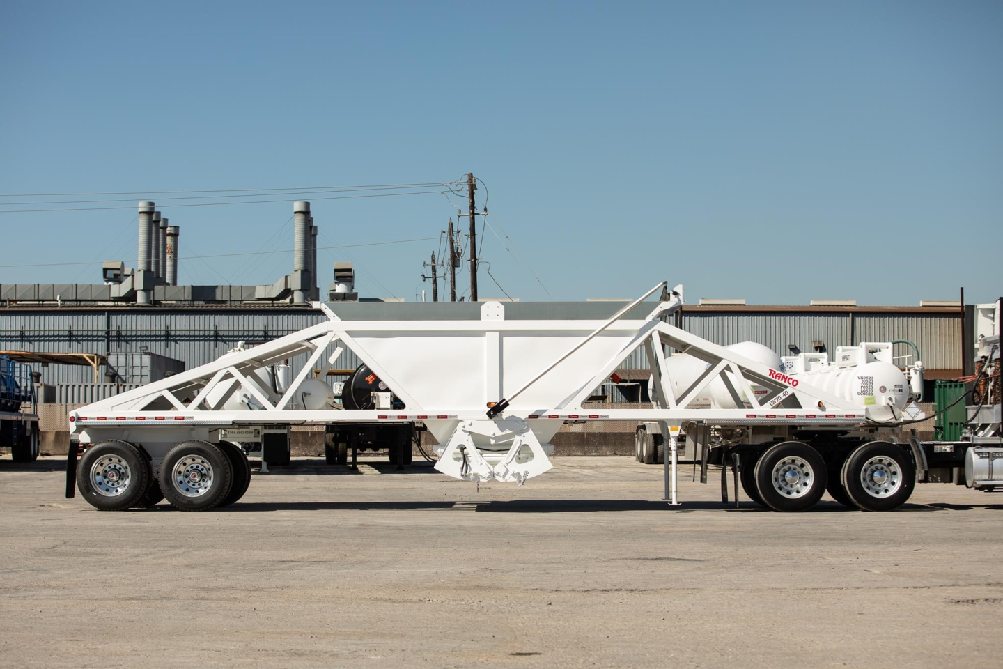 Trailer showing a white Ranco wet sand switchgate bottom dump with a long truss-like frame and multiple axles, side view.
